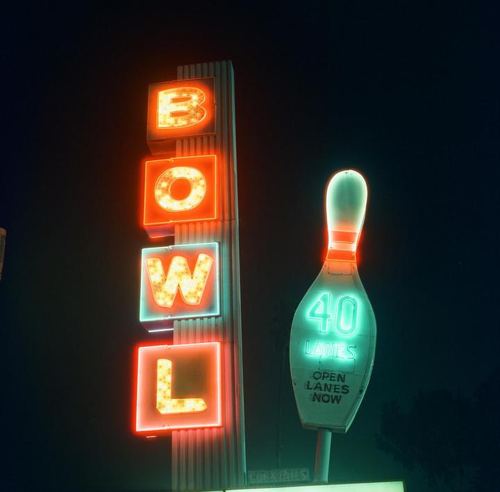 A neon sign for a bowling alley glows brightly against the dark night sky.