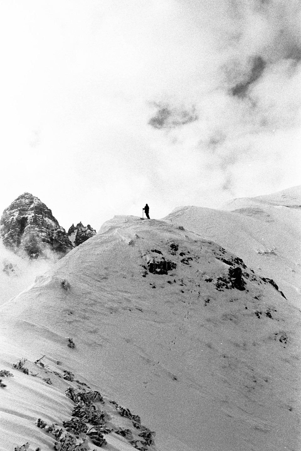 A skier stands on a snowy mountain ridge with a peak in the background.