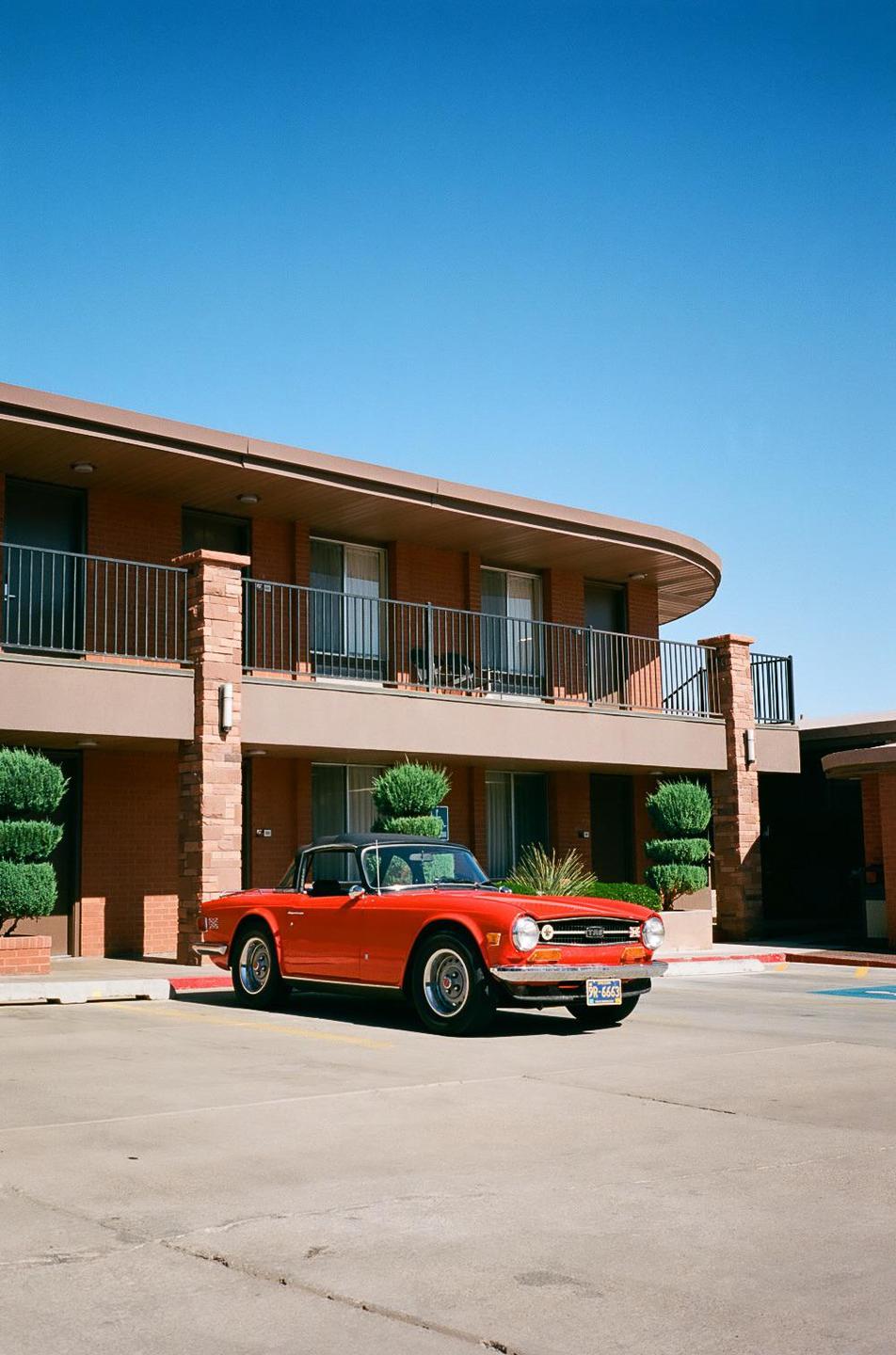A red convertible car is parked in front of a two-story motel building with balconies.