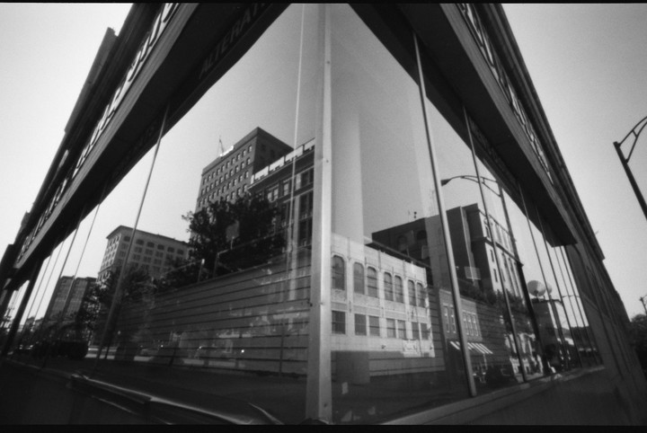 A wide-angle, low-angle black and white shot of a building with large windows reflecting other buildings and the sky.