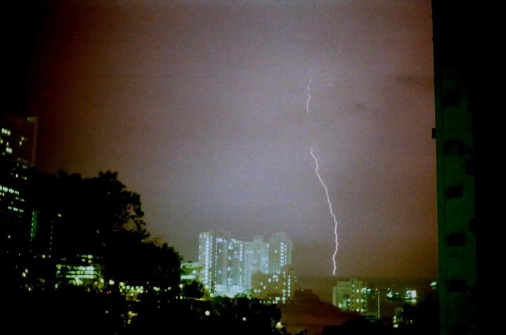 A bolt of lightning strikes in the distance over a city at night.