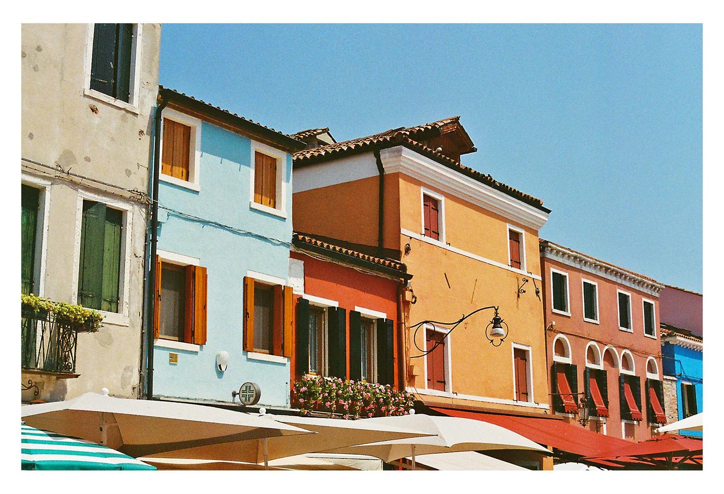 A row of colorful buildings with awnings and umbrellas in Burano.