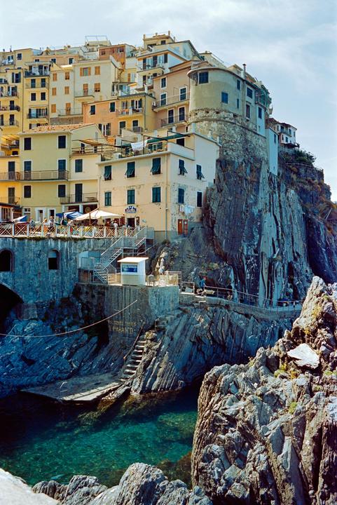 Colorful buildings are built into a cliff overlooking a clear blue body of water.