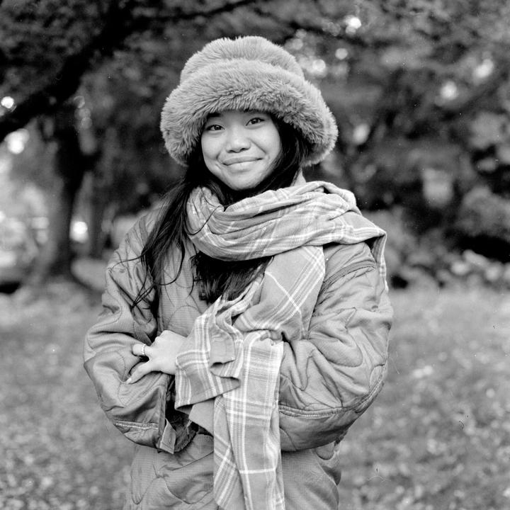A young woman wearing a fur hat and plaid scarf smiles at the viewer.