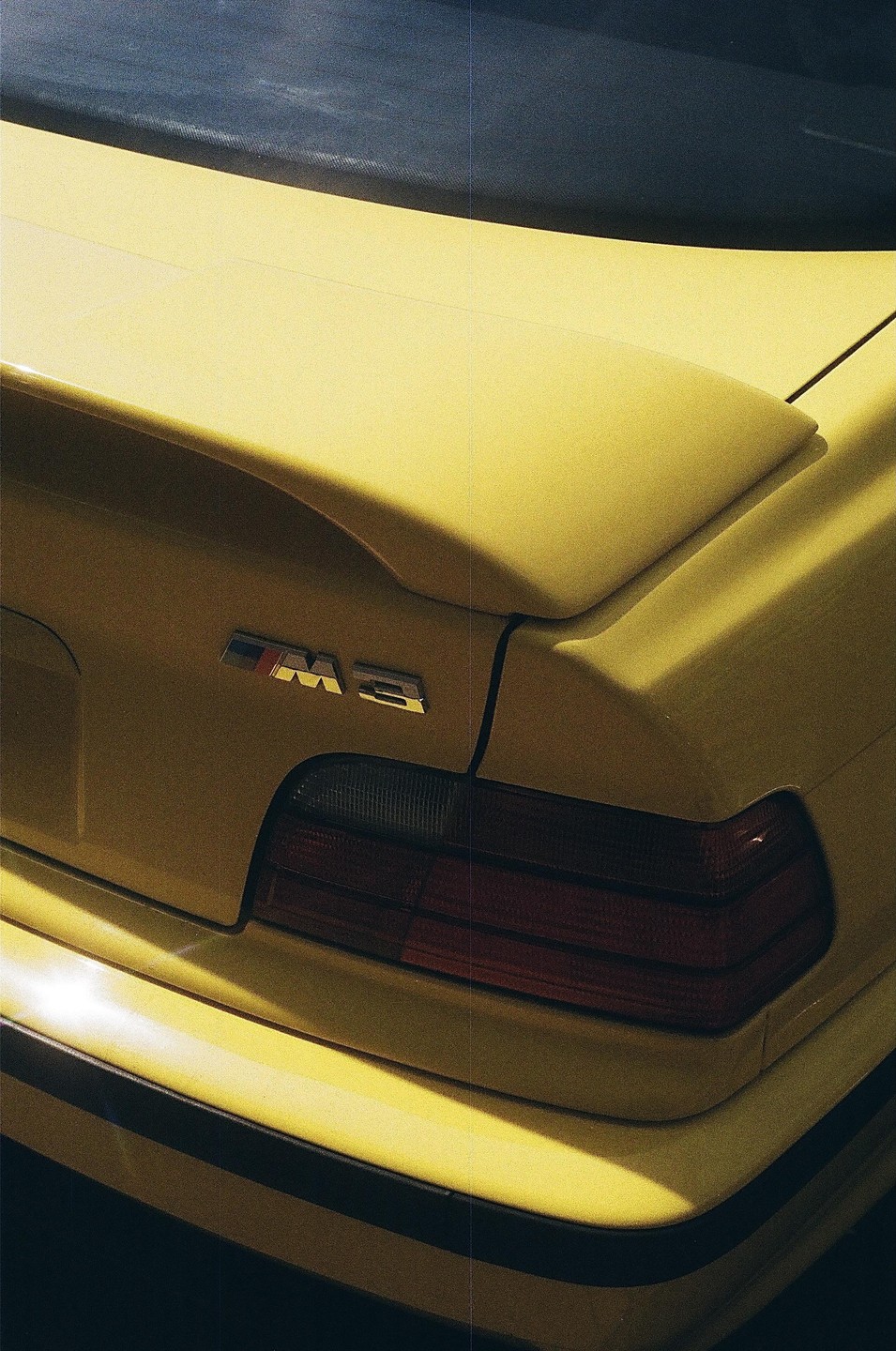 The rear of a yellow car with a spoiler and an M3 emblem is shown.