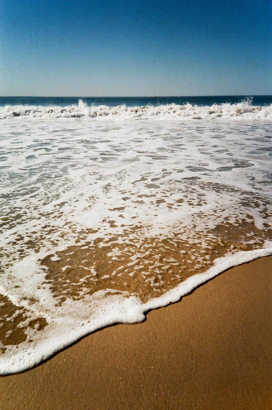 Waves crash on a sandy beach under a clear blue sky.