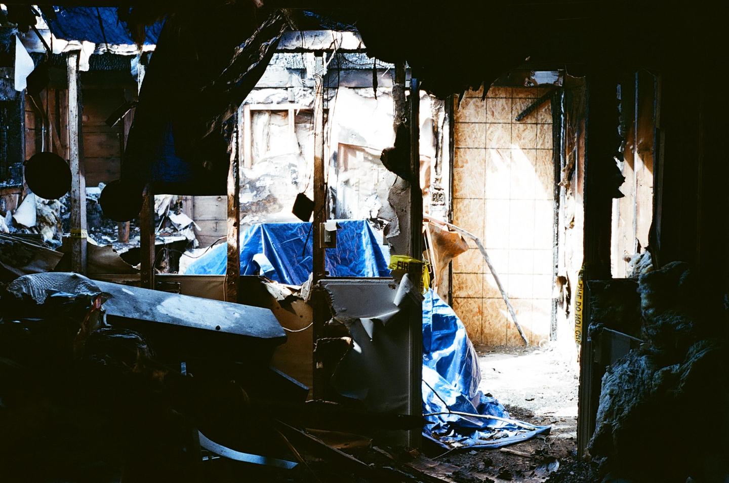 Sunlight streams into a destroyed room with blue tarps covering parts of the floor and walls.
