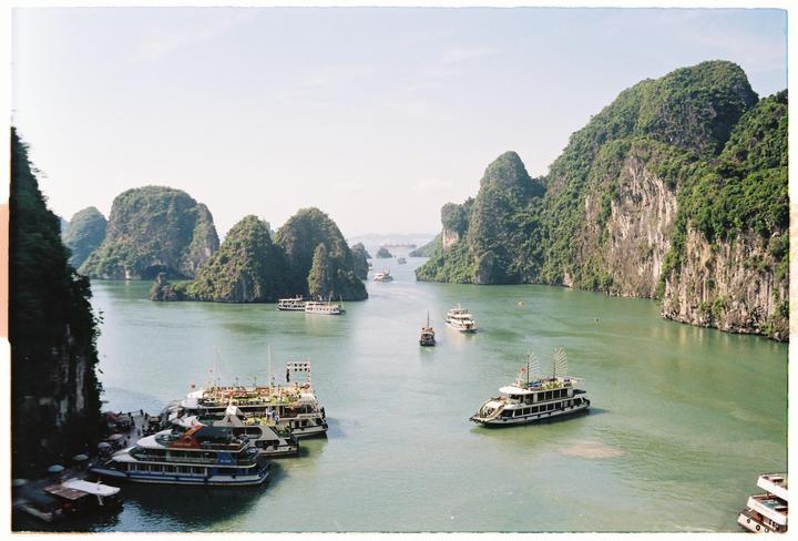 Several boats are visible on the water surrounded by large, tree-covered rock formations.