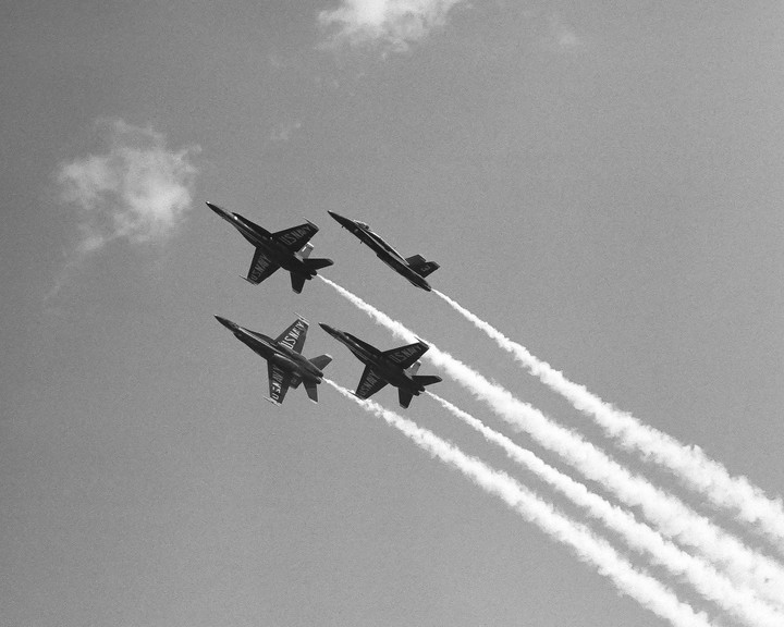 Four fighter jets fly in formation across a cloudy sky, leaving white contrails behind them.