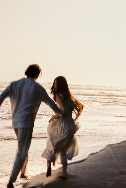 A couple runs along the water's edge on a beach at sunset.