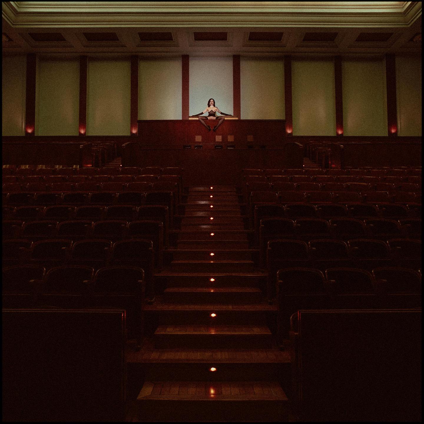 A woman sits on a ledge above rows of empty seats in a cinema.