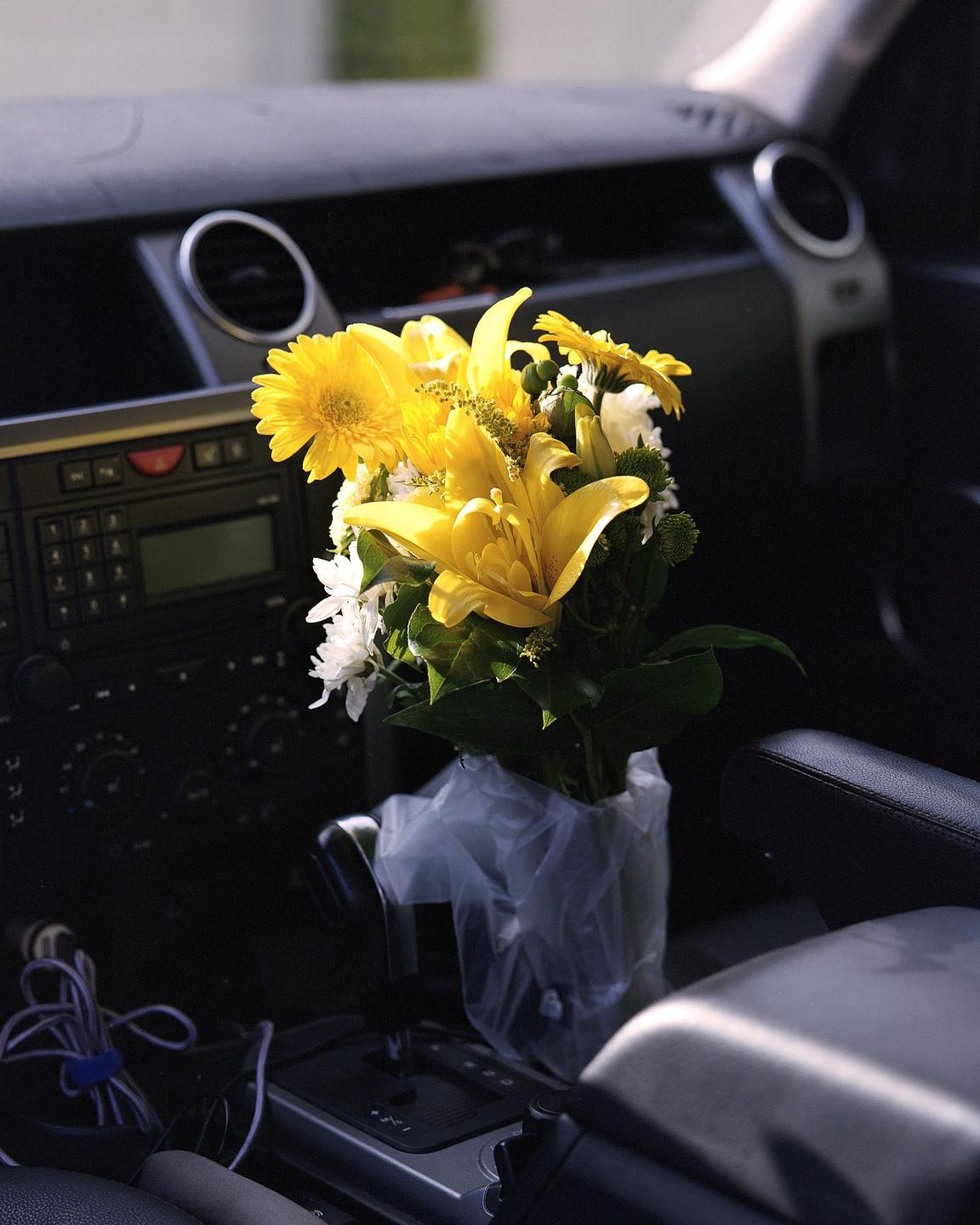 A bouquet of yellow and white flowers sits in the center console of a car.