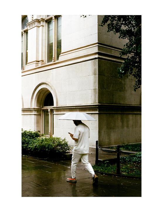 A man holding an umbrella walks past a stone building on a wet street.