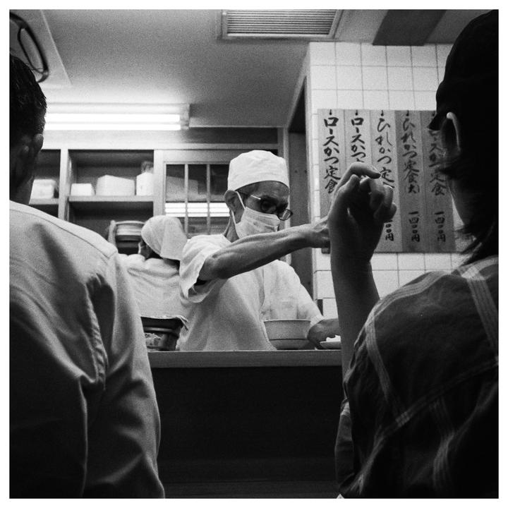 A chef wearing a face mask and glasses serves food to customers at a counter.