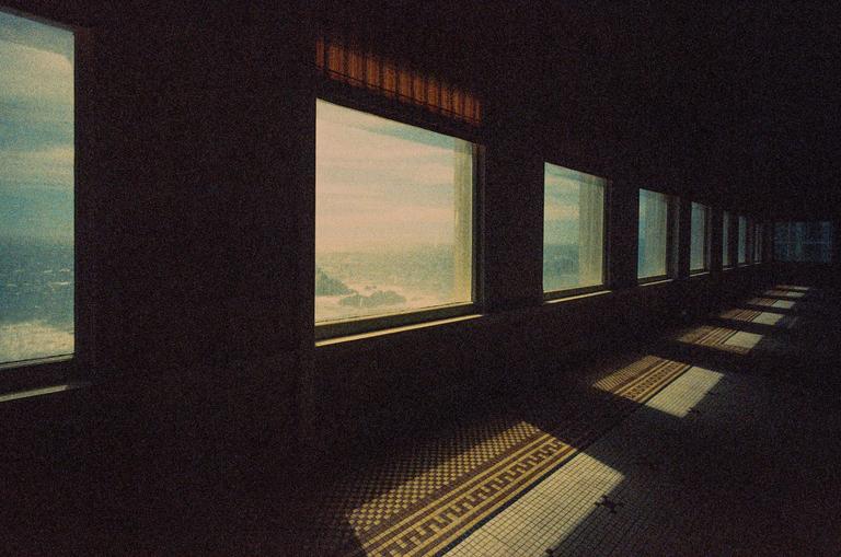 Sunlight streams through a row of windows onto a tiled floor in an abandoned diner.