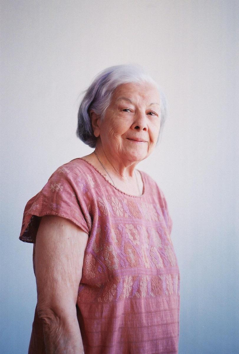 A woman with short gray hair and a pink embroidered shirt smiles at the viewer.