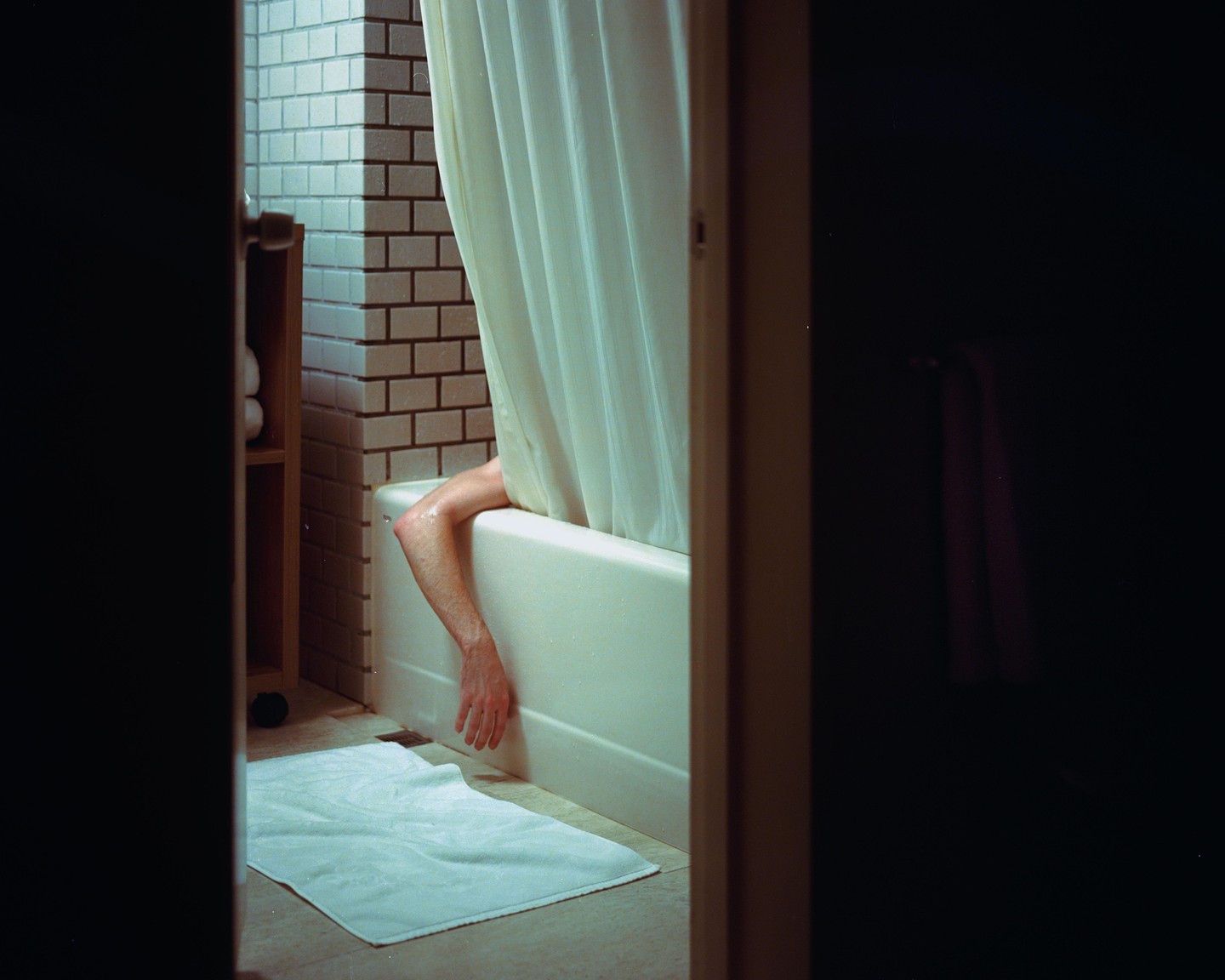 A person's arm hangs over the side of a bathtub with a shower curtain drawn.