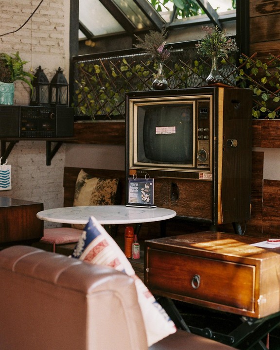 An old television set sits on a wooden cabinet next to a small round table and a leather sofa.