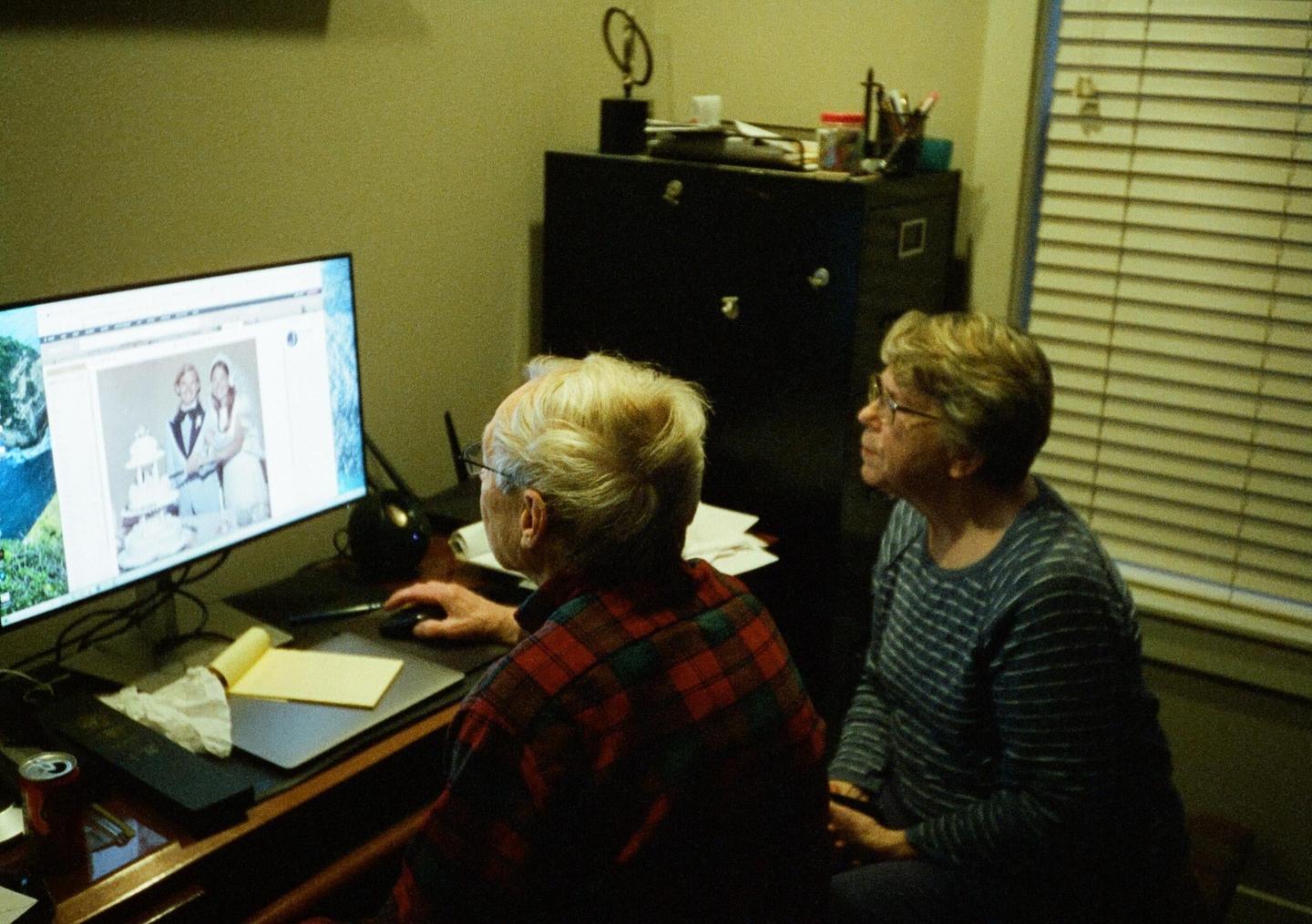A man and a woman are looking at a computer screen displaying a wedding photo.