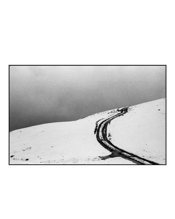 A winding track cuts through a snow-covered hillside under a cloudy sky.