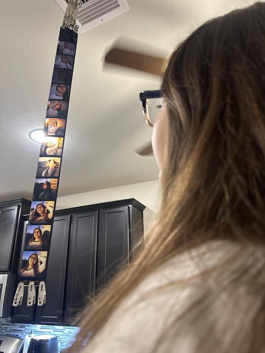A woman looks up at a strip of film hanging from the ceiling, with several portraits visible on the film.