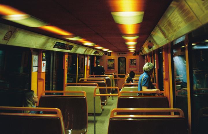 People are riding a subway car with orange and brown seats and bright overhead lights.