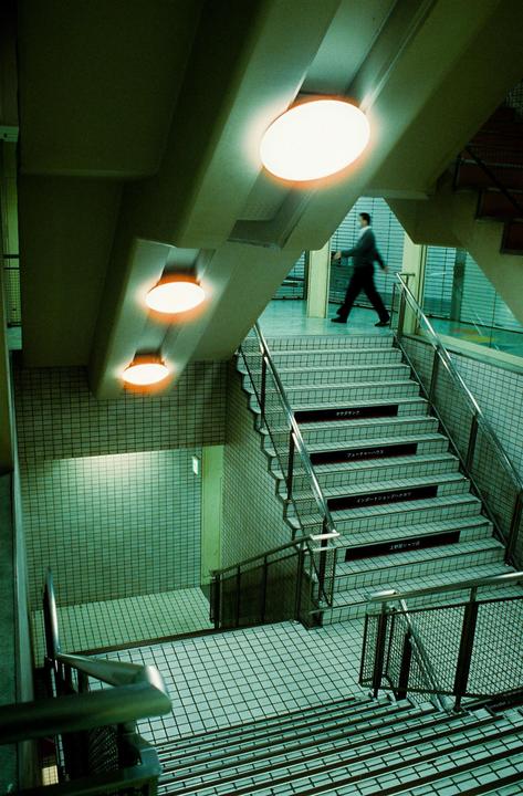 A man walks down a tiled staircase illuminated by three round lights on the ceiling.