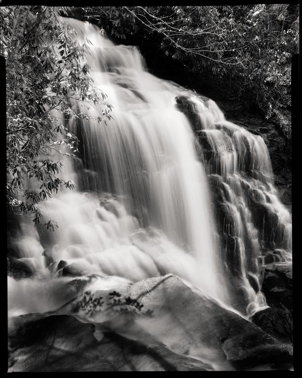 A waterfall cascades over rocks, surrounded by foliage.