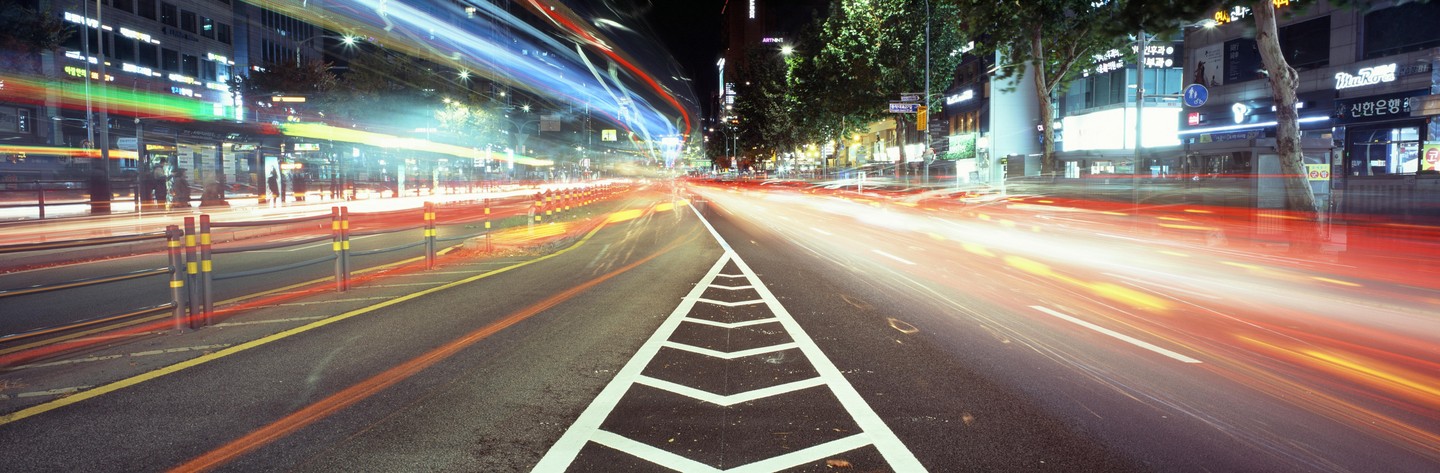Light trails from vehicles illuminate a city street at night.
