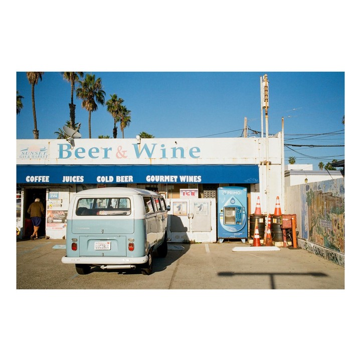A light blue and white van is parked in front of a store with a blue awning that reads "Beer & Wine" under a clear blue sky.