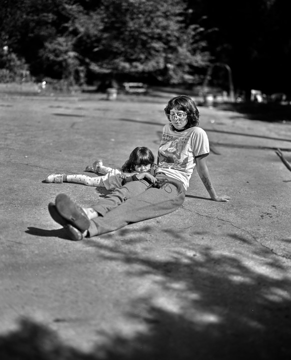 A woman and a child are sitting on the ground in a park.