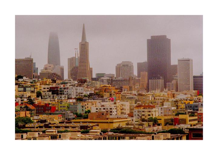 A hazy cityscape of San Francisco shows residential buildings in the foreground and skyscrapers in the distance.