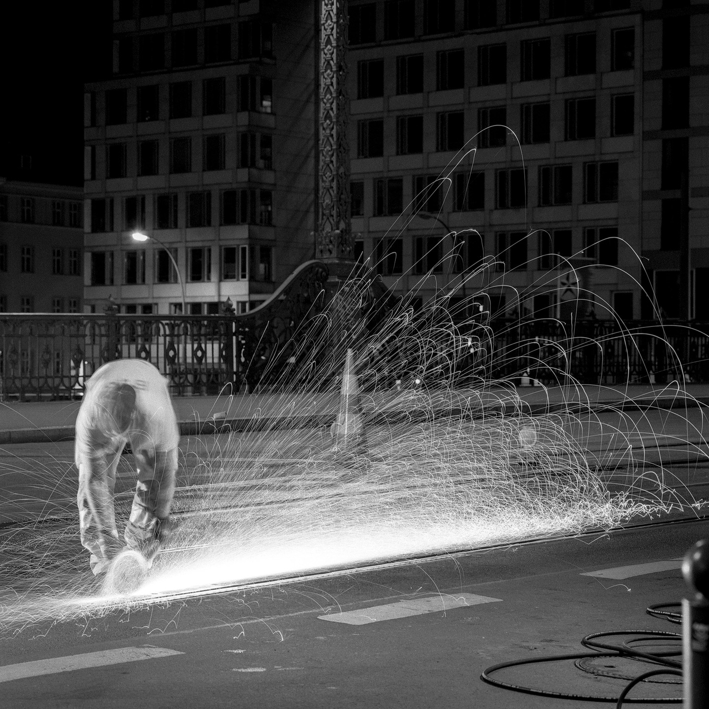 A worker grinds metal on a street at night, creating a shower of sparks.