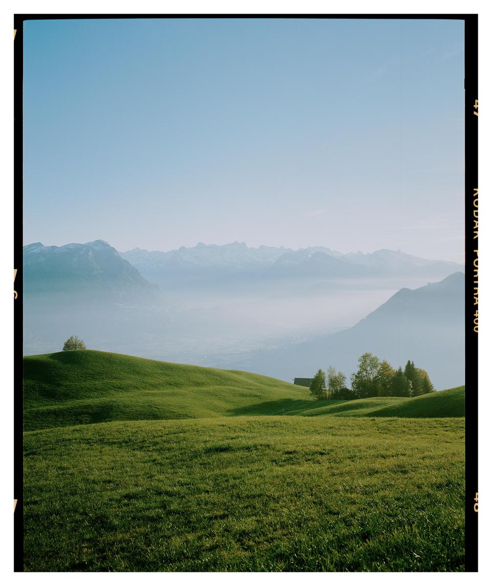 Green rolling hills are visible in the foreground, with a valley and mountains in the background.