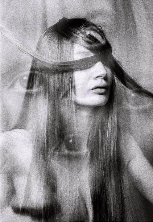 A woman with long hair has a strand of hair covering her eyes in a black and white portrait.