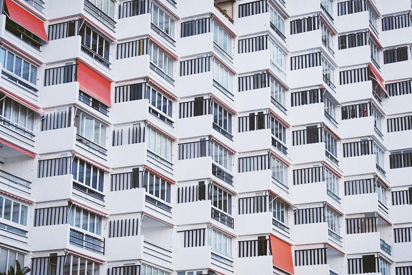 A white apartment building with many balconies and red awnings is shown from an upward angle.
