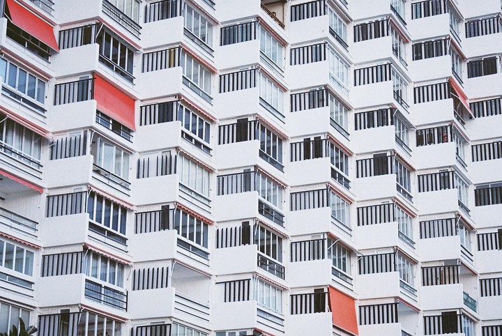 A white apartment building with many balconies and red awnings is shown from an upward angle.