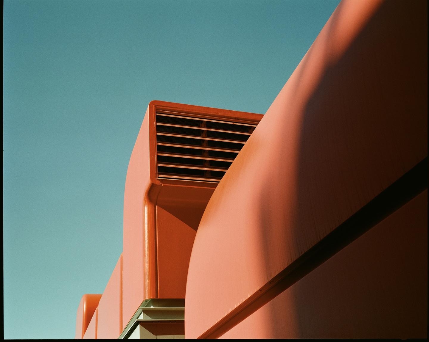 A salmon-colored building with a vent is shown against a clear blue sky.
