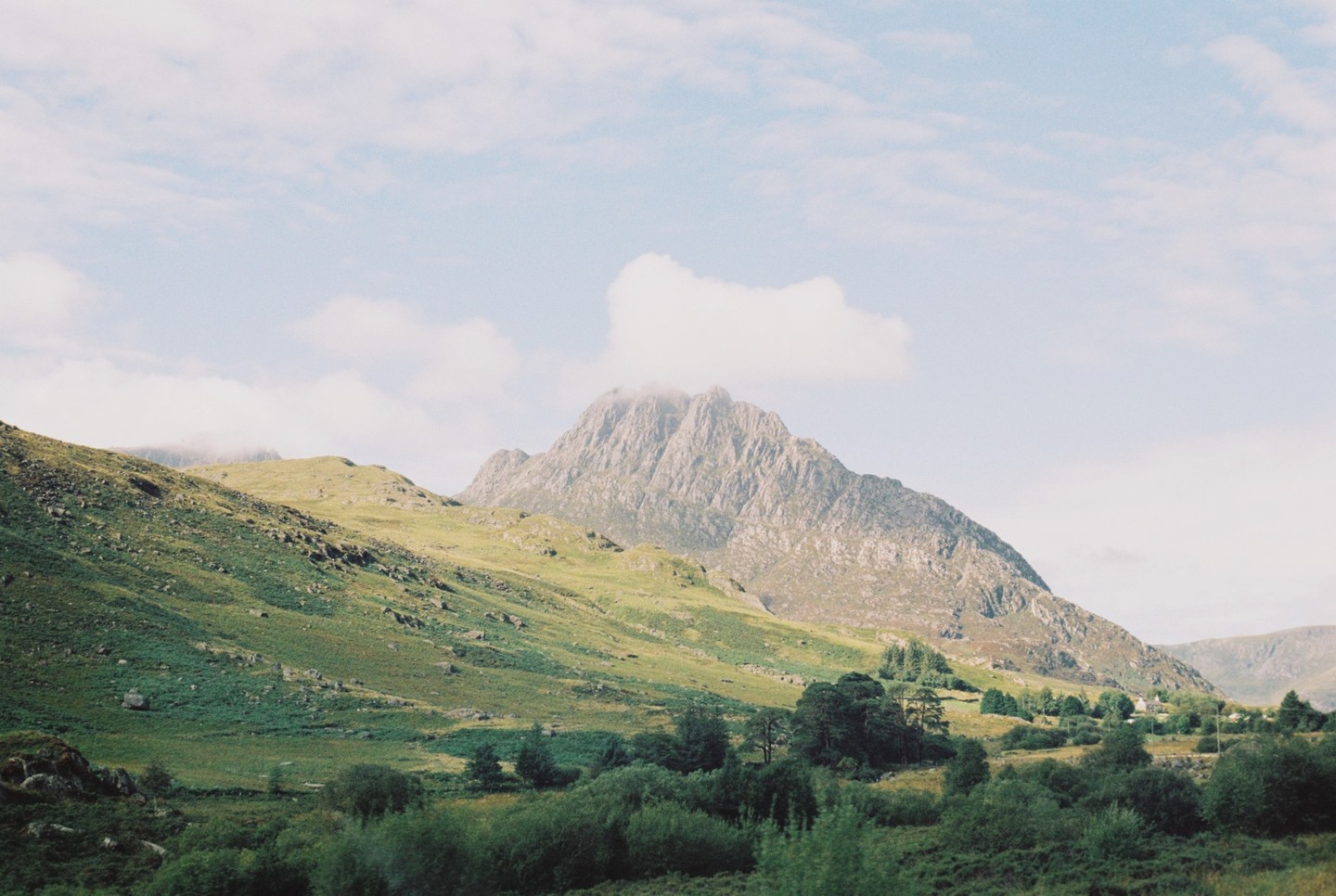 A valley with green hills and a large mountain under a cloudy sky.