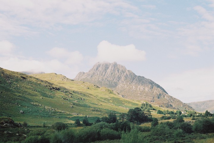 A valley with green hills and a large mountain under a cloudy sky.