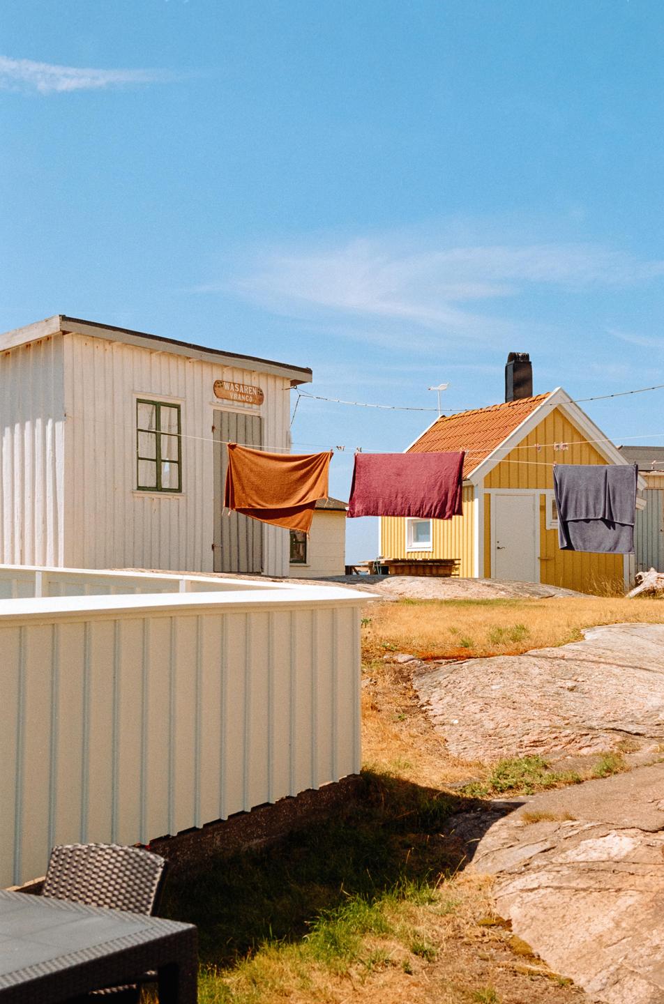 Laundry hangs on a clothesline between two small houses on a sunny day.