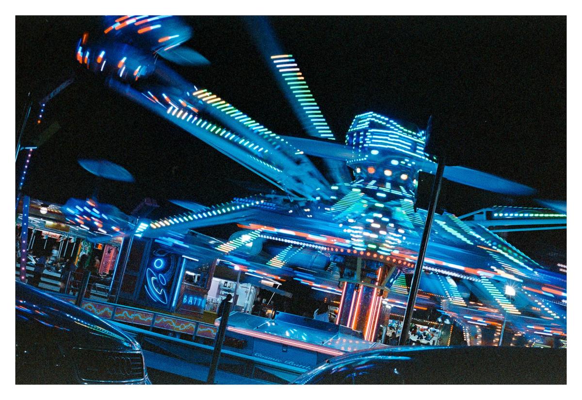 A brightly lit amusement park ride spins at night, creating streaks of light.