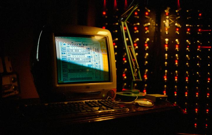 A computer monitor displays a graphic interface with a keyboard and mouse in front of it, next to a green desk lamp and a wall of red lights.
