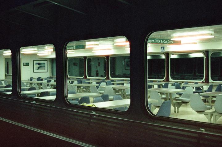 A view through a window shows an empty room with tables and chairs, illuminated by fluorescent lights.