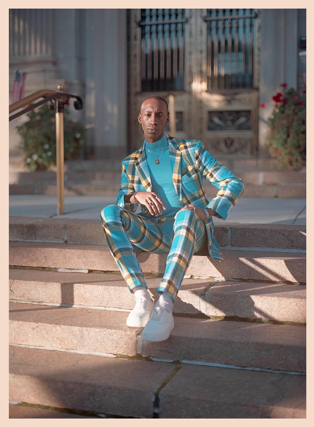 A man in a plaid suit sits on stone steps in front of a building.