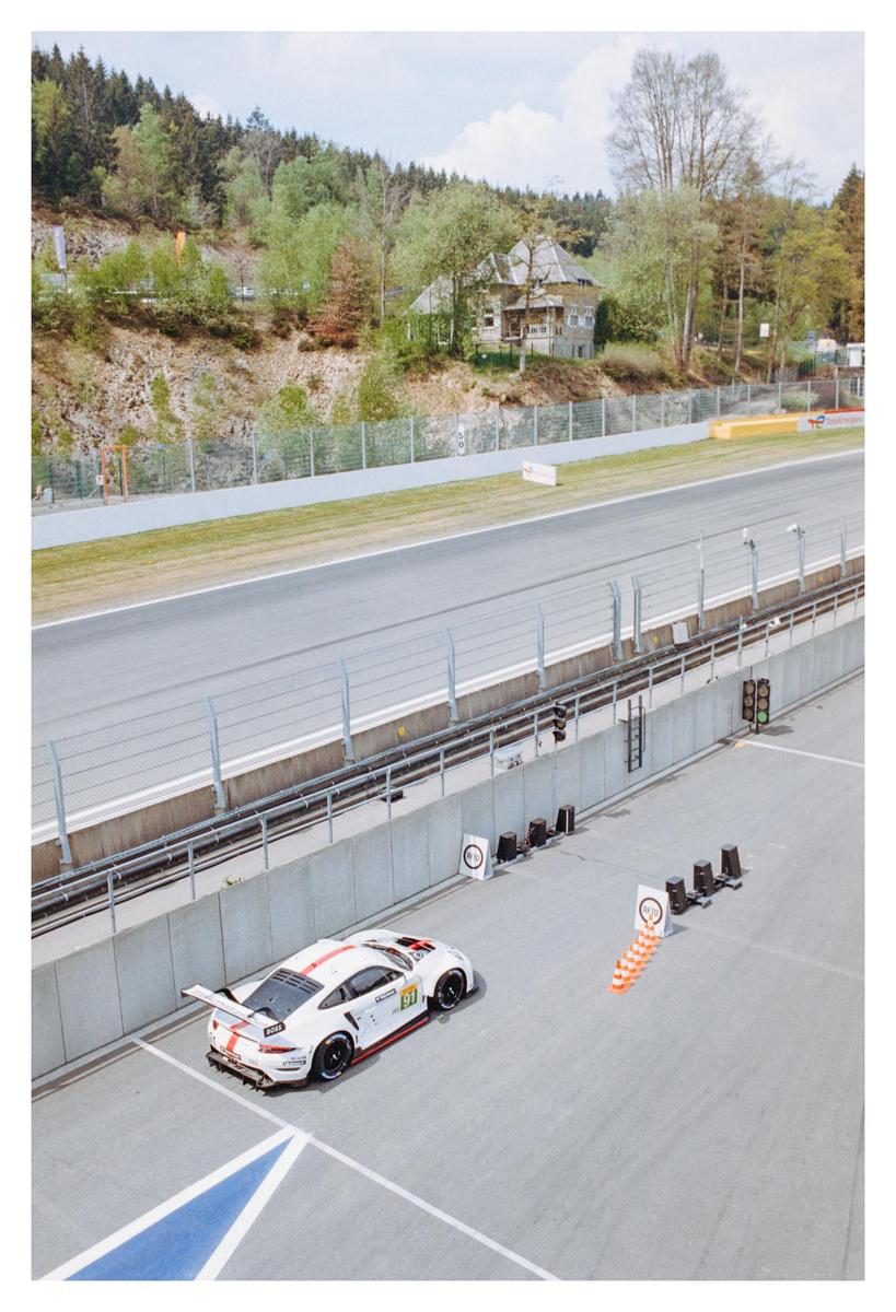 A white race car with red stripes is parked on a race track next to orange traffic cones.