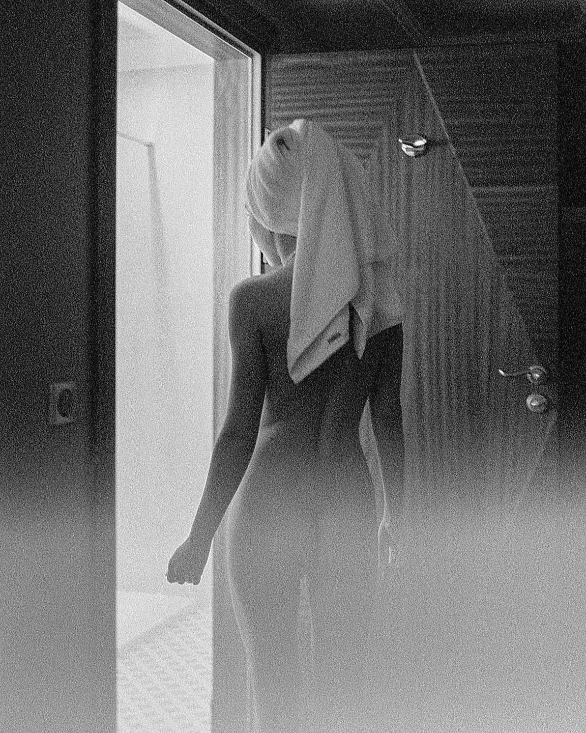 A woman with a towel on her head stands in a doorway, her back to the viewer.