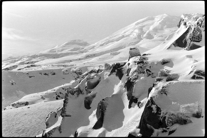 A snow-covered mountain landscape features rocky outcrops and deep shadows.