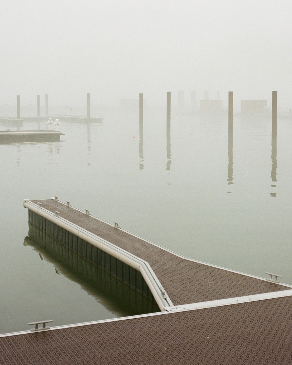 A long dock extends into a foggy body of water with several pilings visible in the distance.