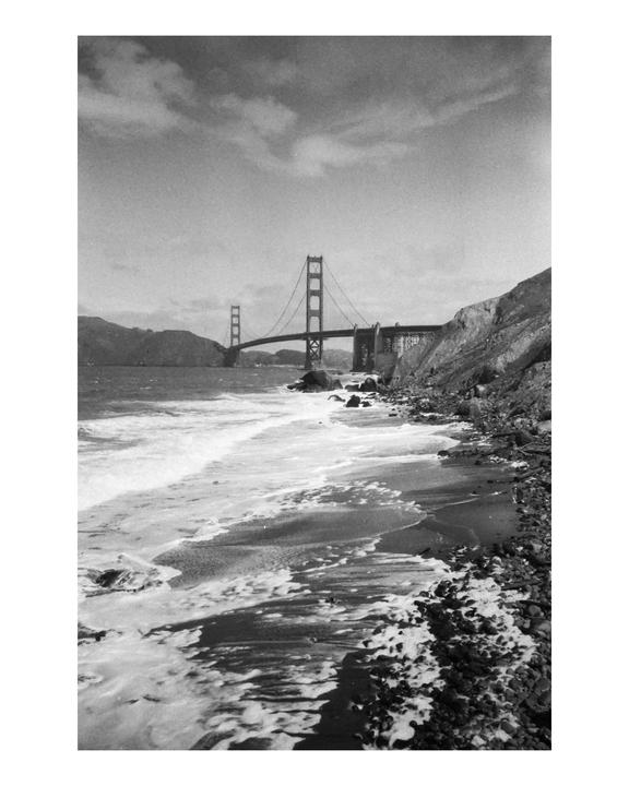 Waves crash on a rocky beach with the Golden Gate Bridge visible in the distance.
